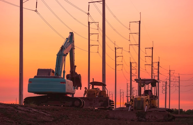 Silhouette of excavator and bulldozer tractors on country road with row of electric poles at sunset