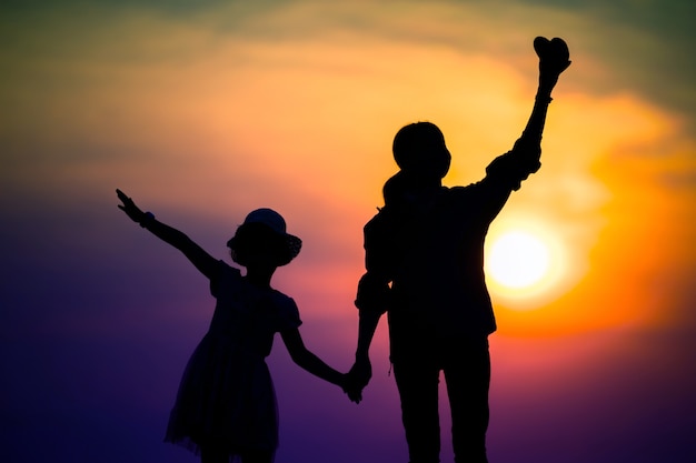 Silhouette of a family with a happy mother playing with a girl in the sunset sky