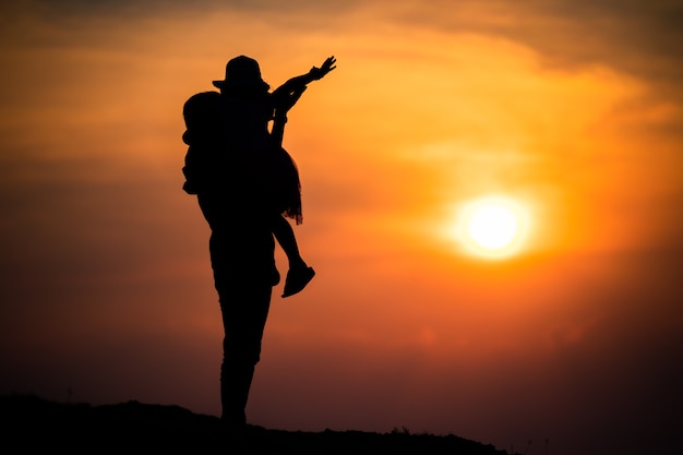 Silhouette of a family with a happy mother playing with a girl in the sunset sky