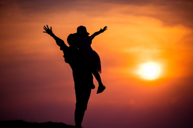 Silhouette of a family with a happy mother playing with a girl in the sunset sky