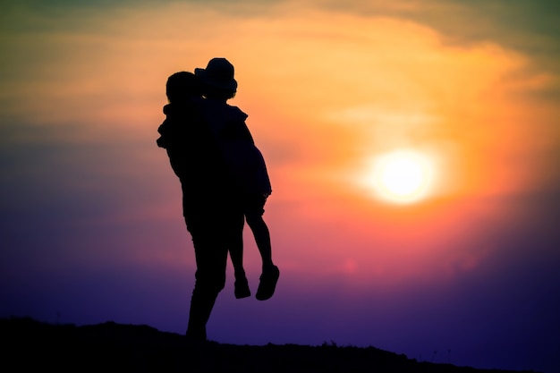 Silhouette of a family with a happy mother playing with a girl in the sunset sky