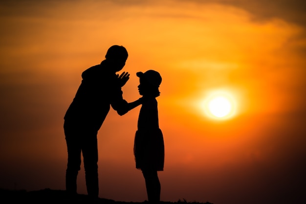 Silhouette of a family with a happy mother playing with a girl in the sunset sky