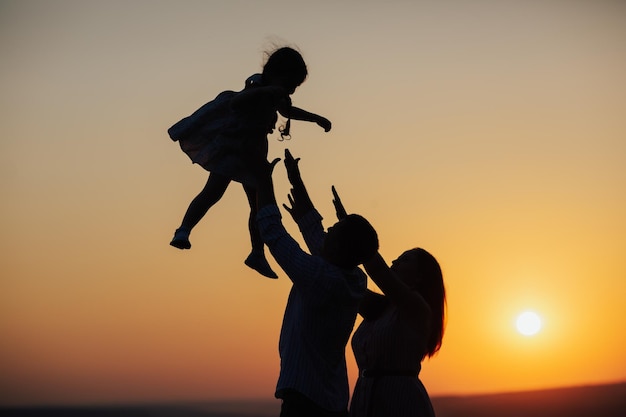 Silhouette of father and mother playing with toddler daughter at sunset