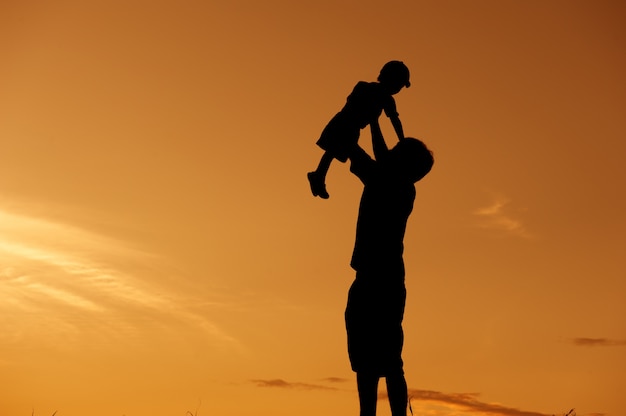 silhouette of a father and son playing outdoors at sunset 