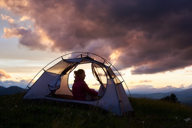 Silhouette of a female camper in the mountains on sunset