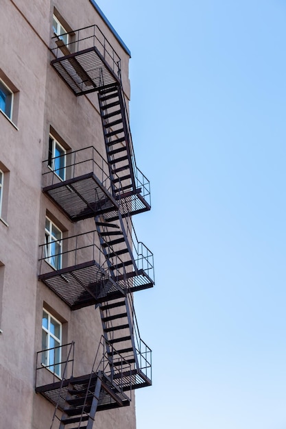 Silhouette of a fire escape on a highrise building against a blue sky with clouds