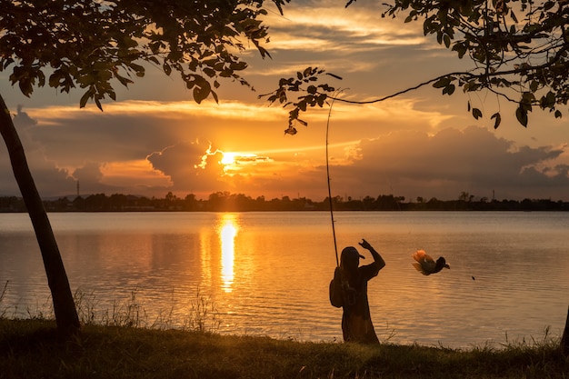 Silhouette of fisherman fishing on river side in sunset