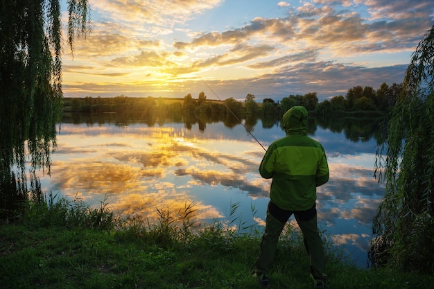 Silhouette of fisherman with fishing rod at sunset by lake