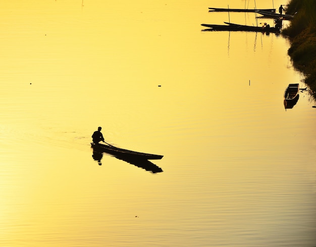 Silhouette of fishermen Take a small fishing boat to the river at sunset yellow background