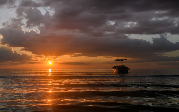 Silhouette fishery boats in the sea with sunset warm low lighting and dark shadow.