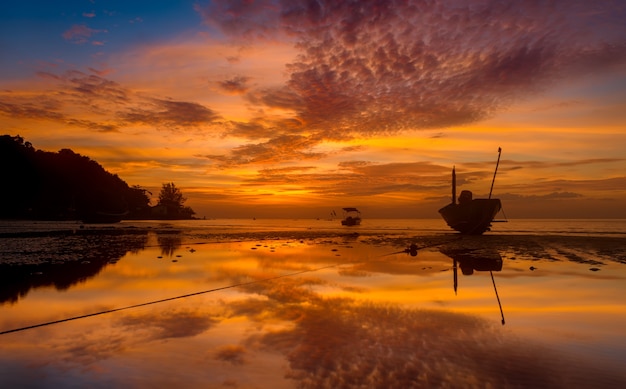 Silhouette fishery boats in the sea with sunset warm low lighting and dark shadow.