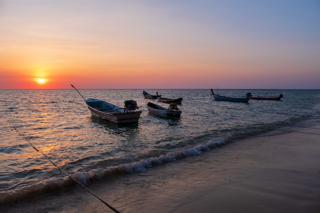 Silhouette of fishing boat on tropical beach at sunset. 