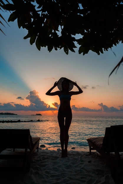 Silhouette of fit girl posing on tropical beach on ocean shore with sunset in Maldives with skyline