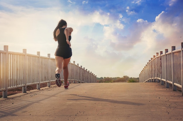 silhouette of fit woman jogging workout across the bridge while marathon practicing at the sunset