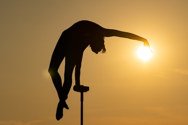 Silhouette of flexible acrobat doing handstand on the dramatic sunset background