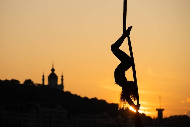 Silhouette of a flexible woman acrobat on aerial silk during a sunset on Kiev city. concept of freedom and peace.