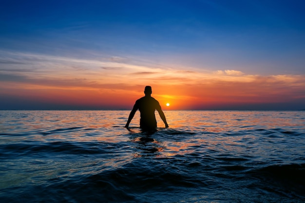 Silhouette of freedom Man Raising Hands in blue sea beach at sunset