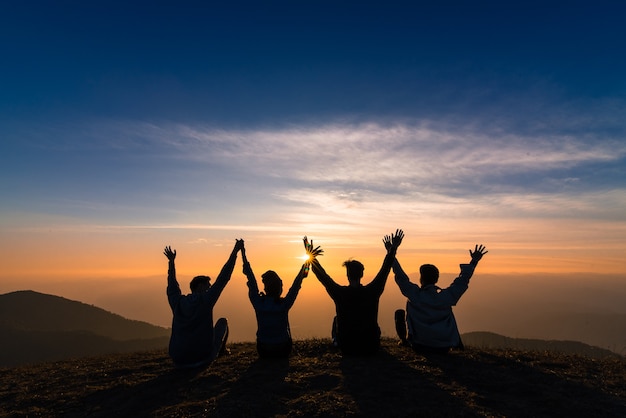 silhouette of friends shake hands up and sitting together in sunset happiness