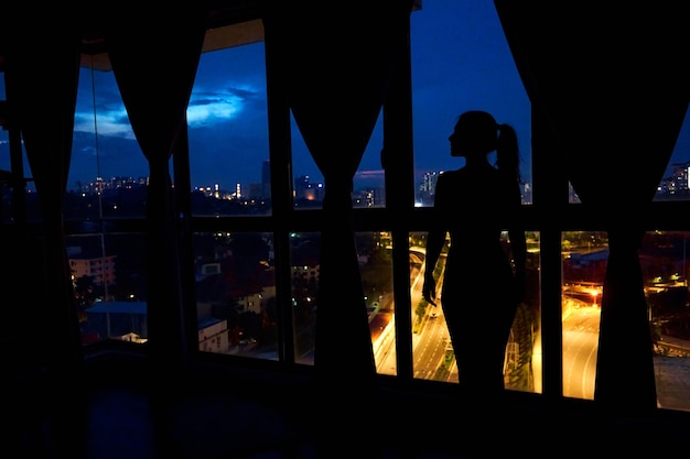 The silhouette of a girl against a stainedglass window looks at the night city