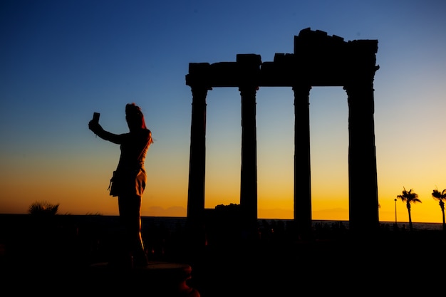 Silhouette of girl making selfie in Temple of Apollo at sunset