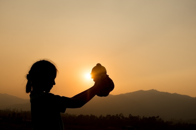 silhouette of girl standing alone and hand holding teddy bear at a sunset time