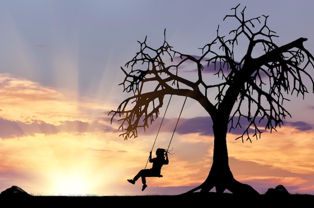 Silhouette of the girl on the swing near a tree at sunset