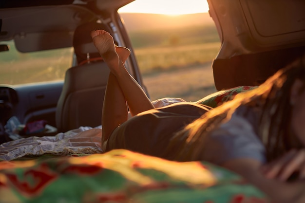 Silhouette of a girl who lies in the car on a blanket against the backdrop of the setting bright sun...