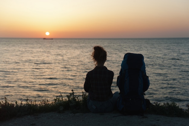 Silhouette of a girl with a backpack on the sunset background