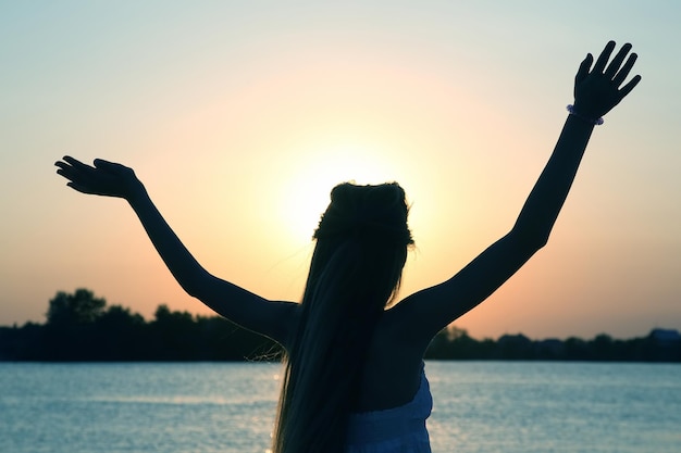 Silhouette of a girl with her hands up against a sunset on the water