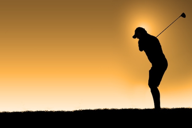 Silhouette of a golfer taking a the first hit of the day with an orange sky background