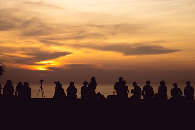 Silhouette group of people sitting look at sunset light with orange sky at Phuket, Thailand