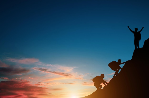 Silhouette group of tourist with backpack is climbing a cliff alone at sunrise He had an effort to climb all the way to the top of the mountain and he had to succeed