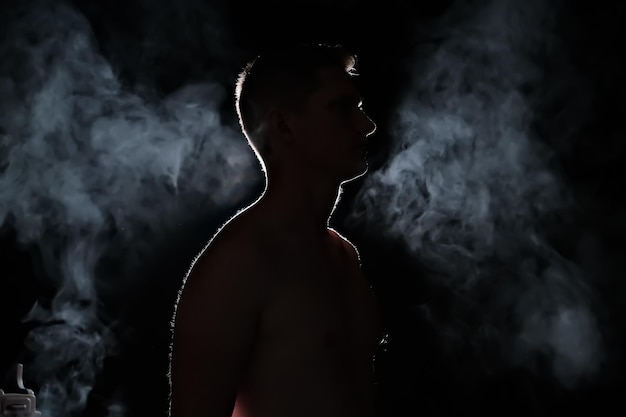 Silhouette of a guy men in the dark smoke steam man in a dark room