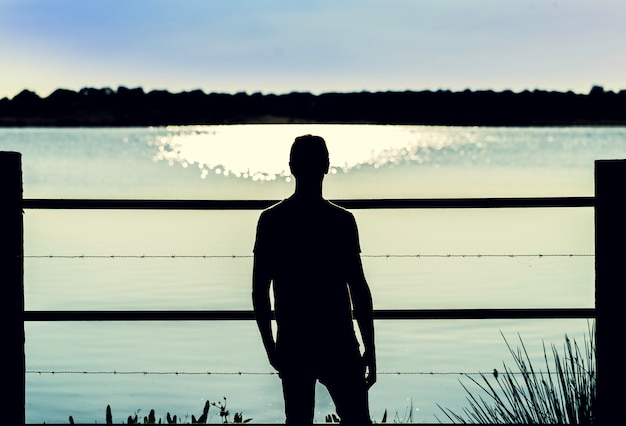 Silhouette guy standing  in the barbed wire fence looking the water of the marsh