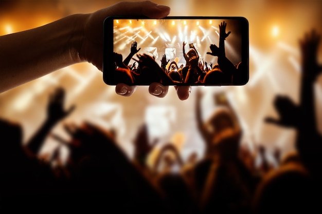 Silhouette of hand using camera phone to take pictures and videos at pop concert, festival.