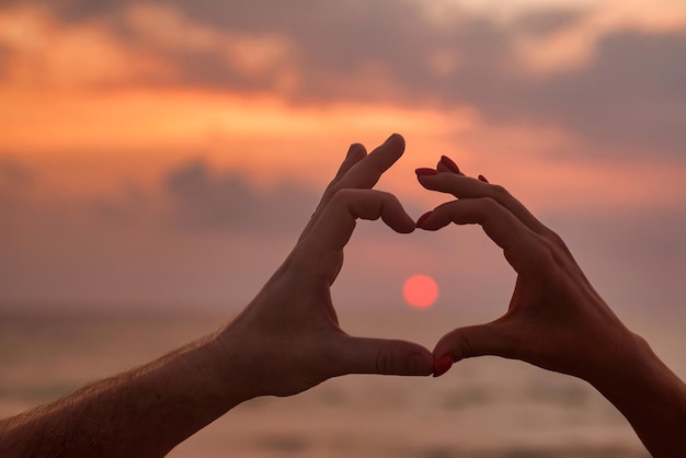 Silhouette hands of couple are lovely heart shape with sunset on through hand Woman and man hands in heart shape with sunrise