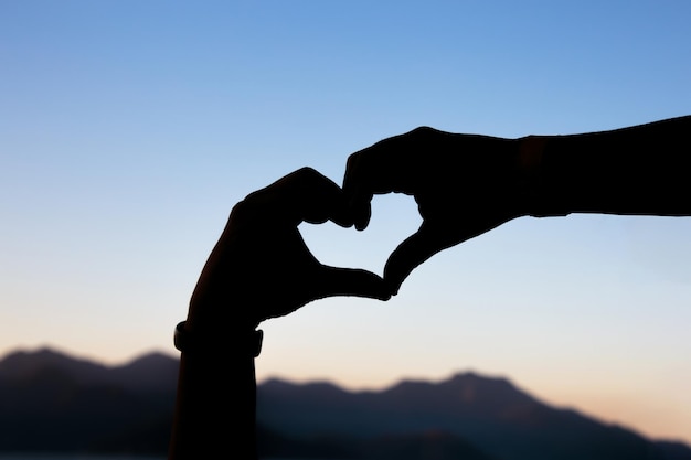 silhouette of hands in the shape of a heart against a beautiful colorful late afternoon sky