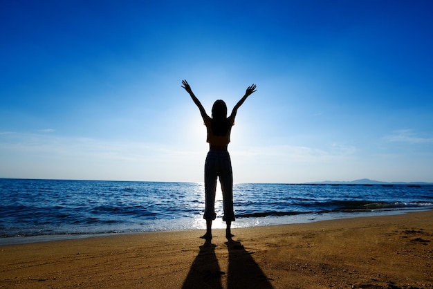 Silhouette happy young woman enjoying freedom with open hands on sea at sunset