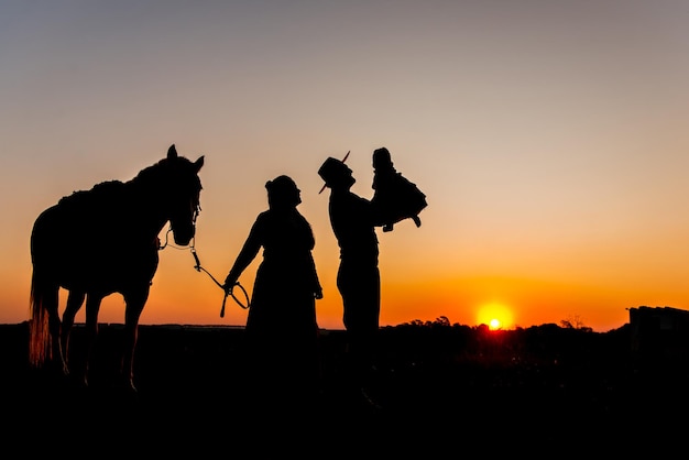 Silhouette of horse and gaucho family at sunset in the countryside