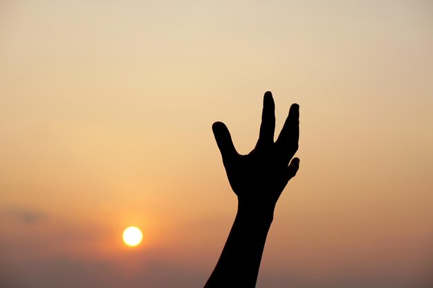 Silhouette of human hand raised to make a wish sunset background