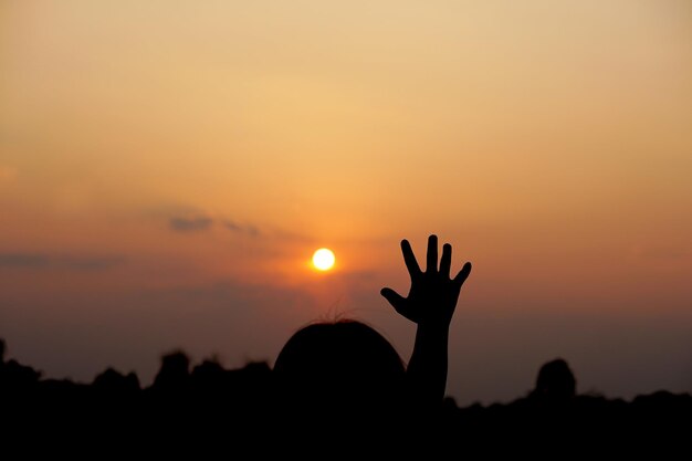 Silhouette of human hand raised to make a wish sunset background