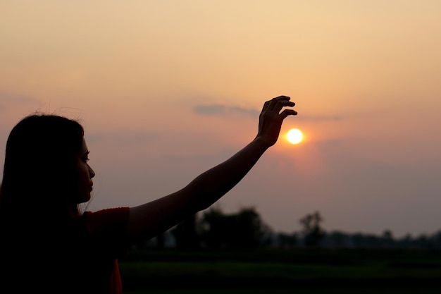 Silhouette of human hand raised to make a wish sunset background