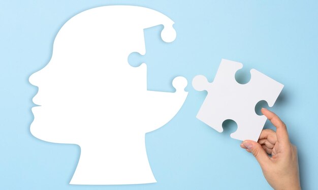 Silhouette of a human head holding a puzzle piece on a blue background representing mental health