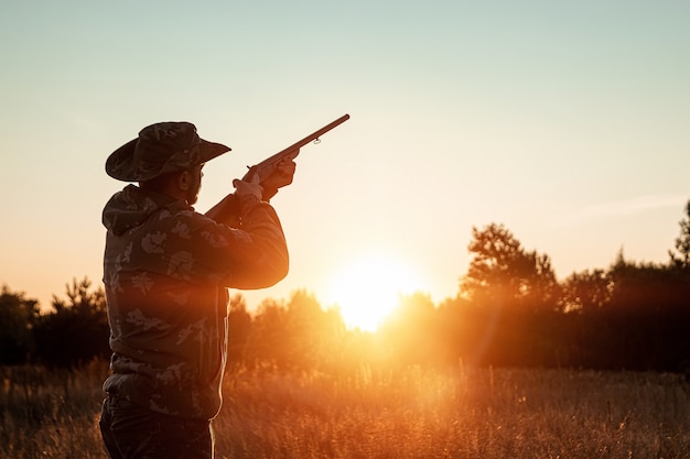 Silhouette of Hunter in a cowboy hat with a gun in his hands on a beautiful sunset