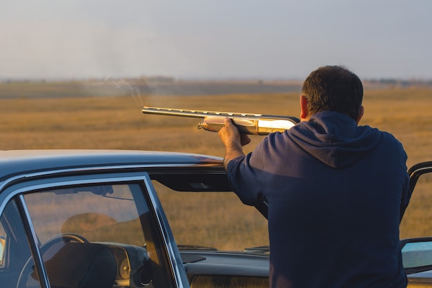 Silhouette of a hunter with a gun in the reeds against the sun, an ambush for ducks with dogs