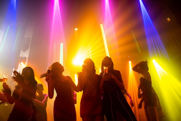 Silhouette image of people dance in disco night club to music from DJ on stage