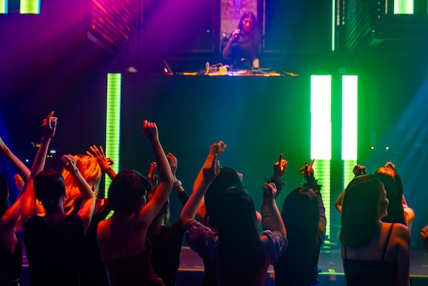 Silhouette image of people dance in disco night club to music from DJ on stage