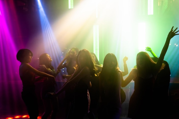 Silhouette image of people dance in disco night club to music from DJ on stage