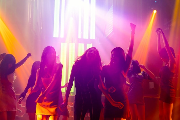 Silhouette image of people dance in disco night club to music from DJ on stage