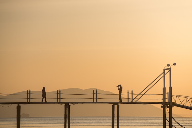 a silhouette of lovers taking pictures on the bridge over the sea of the sunset